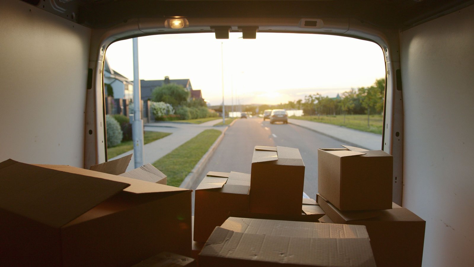 Cardboard parcels inside a delivery van looking towards a suburban road at sunset